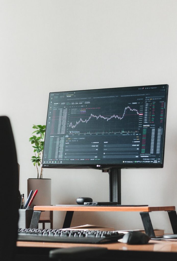 a computer monitor that is showing trading chart is  sitting on top of a wooden desk 